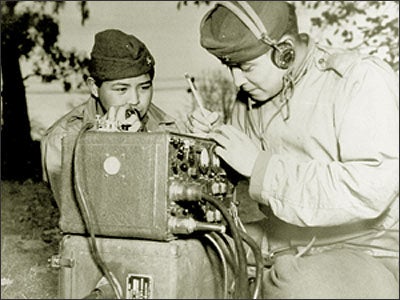 Private First Class Preston Toledo and Private First Class Frank Toledo, cousins and Navajos attached to a Marine Artillery Regiment in the South Pacific, relay orders over a field radio in their native tongue, July 7, 1943. (U.S. Marine Corps photo/National Archives No. 127-MN-57875)