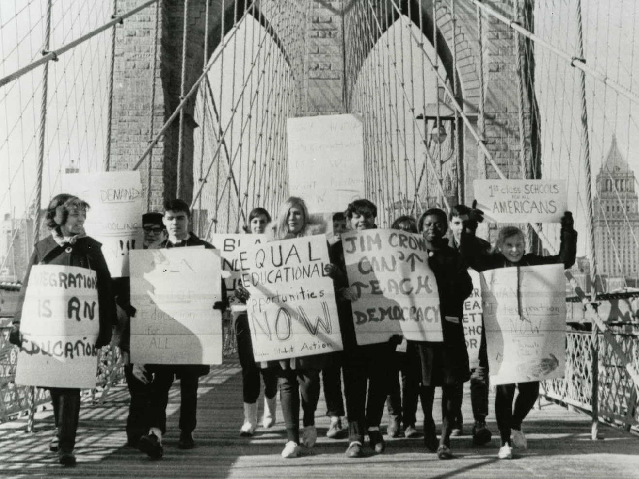 Black and white photo of students protesting segregation in schools as they cross the Brooklyn Bridge in 1964. Holding signs that read "Equal Education Opportunities Now" and "Jim Crow Can't Teach Democracy." 
