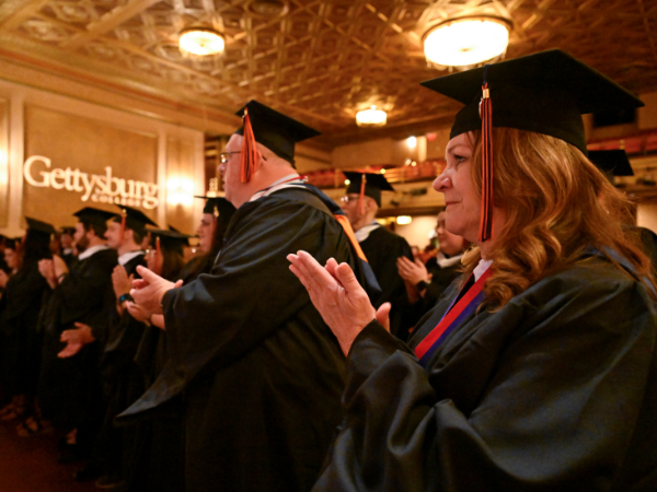View of graduating students in cap and gown in a ballroom with "Gettysburg College" written on a wall in the background
