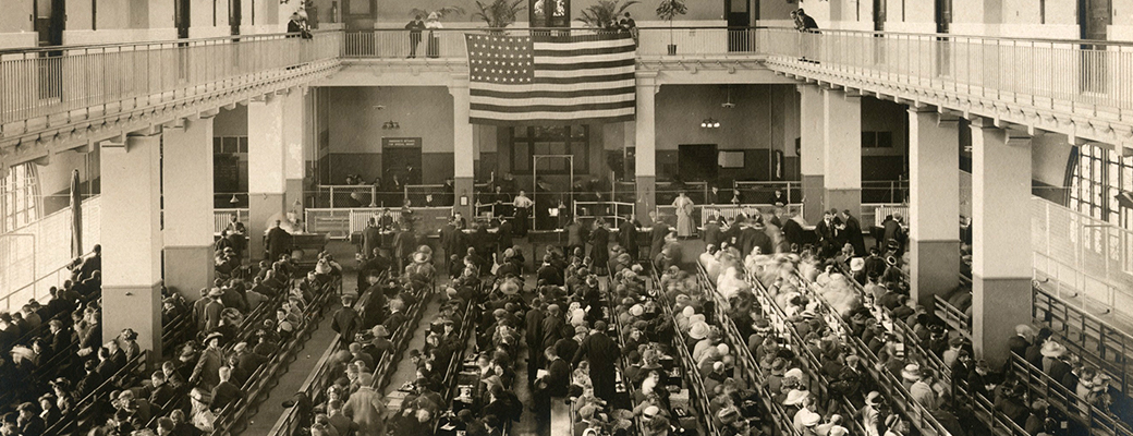 Immigrants seated on long benches, Main Hall, Ellis Island Immigration Station, ca. 1907-1912 (New York Public Library Digital Collections)