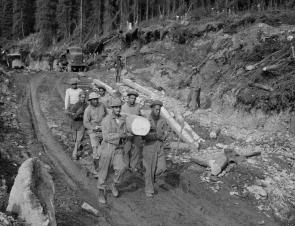 Army engineer troops haul logs down a road while building the Alcan Highway, ca.