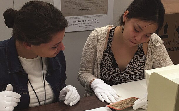 Two Gilder Lehrman Interns working at the Collection, examining a historical photograph while wearing white gloves