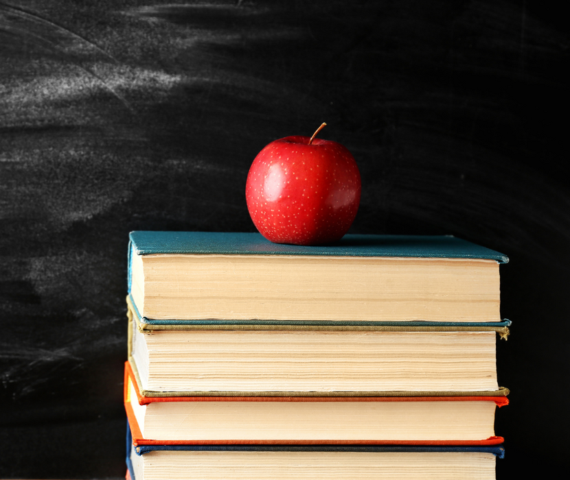 Apple on a stack of books in front of a chalkboard