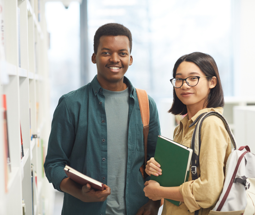 Two students near bookshelf holding books