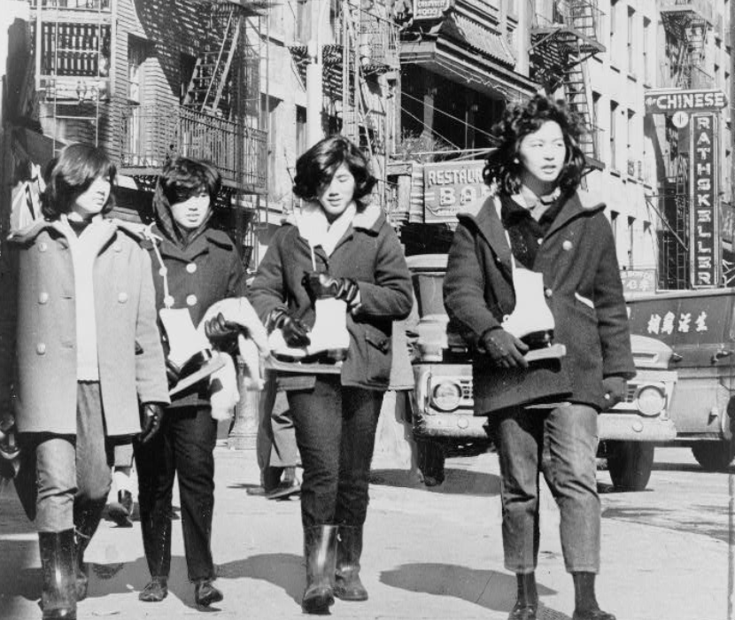 A black and white photograph of four Chinese American young women carrying ice skates in Chinatown.