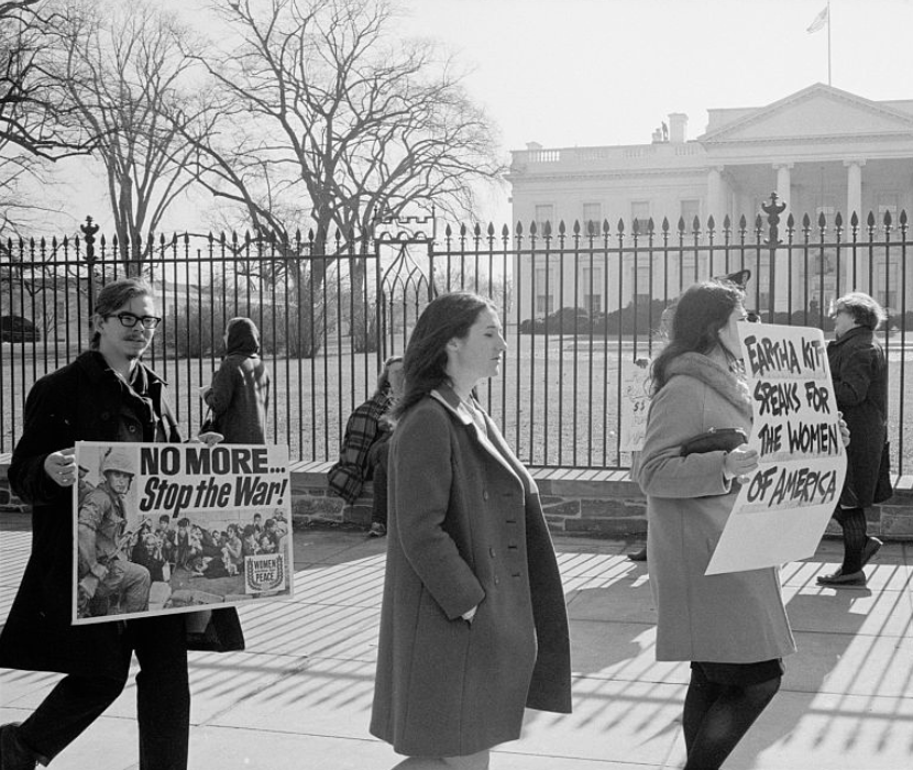 A photograph of anti-Vietnam War demonstrators carrying signs, "No more...Stop the war!", "Eartha Kitt speaks for the women of America", and "Stop the draft", picketing in front of the White House.