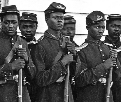 Black soldiers in dark Union Army uniforms, jackets with sashes and epaulets, and caps with a horn embroidered on the bill, looking at the camera while holding their rifles.