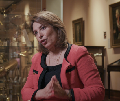 Reyes Calderon speaking in front of portraits and maritime navigational instruments