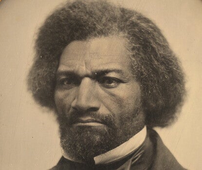 A black-and-white photograph of a finely dressed, bearded, dark-haired Frederick Douglass looking sternly in three-quarter view