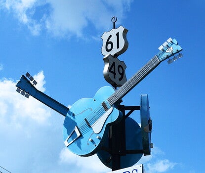 The sign for The Crossroads, featuring a ring of three blue guitars (each facing a different direction) on the bottom and the highways 61 and 49 signs above. 