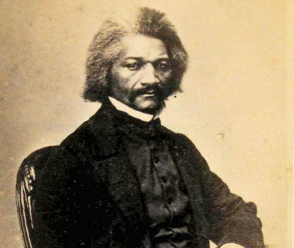 A black-and-white photograph of Frederick Douglass, a Black man in his fifties with graying hair and a serious demeanor staring straight into the camera