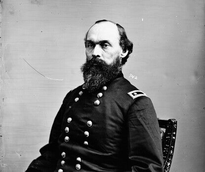 A black-and-white photograph of a White soldier with a heavy dark beard sitting in a chair, wearing a double-breasted Union Army uniform, with a gold bar with two stars on his left shoulder