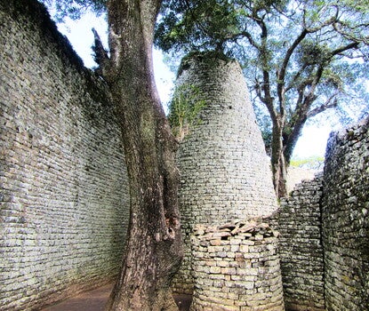 A round stone tower next to a tree, flanked on all sides by stone walls