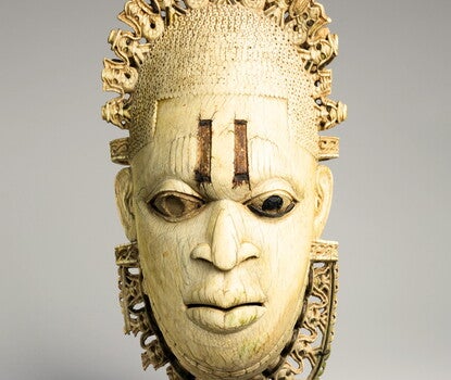 An ivory and metal mask of a woman, with a tiara and necklace
