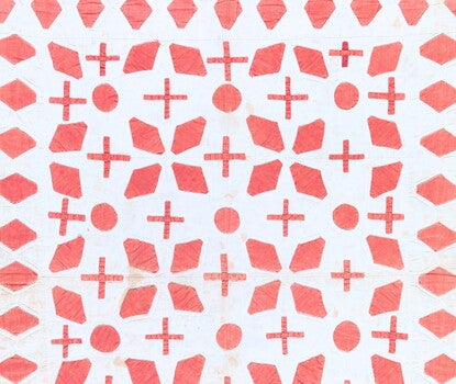 A cream quilted bedcover with appliqued red diamonds, circles, and crosses and edges bound with red