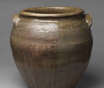 A wide-mouthed brown earthenware jar with two handles and writing inscribed on the surface.