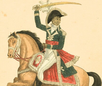 A color print of Toussaint L'Ouverture, a Black soldier, wearing a Haitian cavalry uniform (black hat with a gold frill and white flower, blue jacket with gold trim and epaulets, white pants, and black boots) holding a sword atop a brown horse with a red and gold saddle.