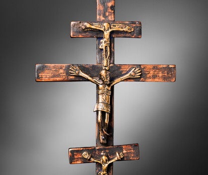 A wooden crucifix sculpture with three crosses stacked vertically, each with a Christlike crucified figure