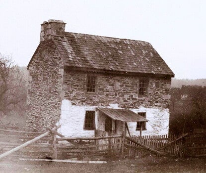 A sepia photograph of a stone house with a shingled roof.