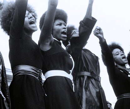 Seven Black women with Afros raising their right fists.