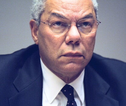 Colin Powell, a gray-haired, bespectacled Black man, wearing a black jacket, white shirt, and polka dot (white dots on black fabric) tie