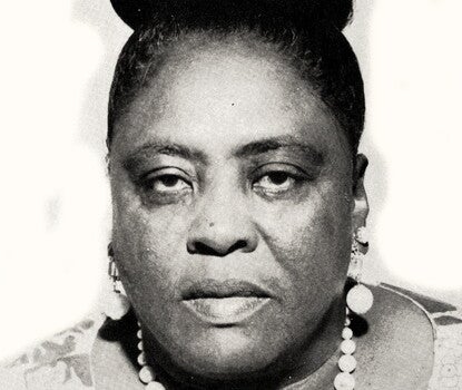 Black and white headshot of a Black woman with her hair in a bun, wearing a white necklace and looking directly at the camera.
