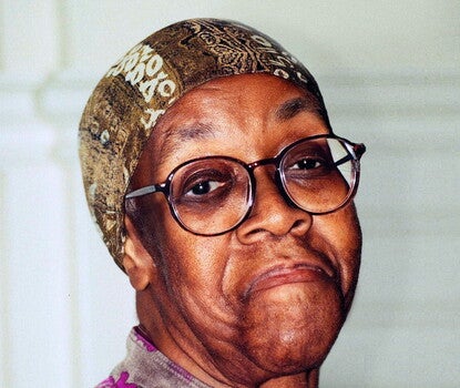 Gwendolyn Brooks, a bespectacled Black woman, wearing a brown and magenta floral shirt and a brown head cover.