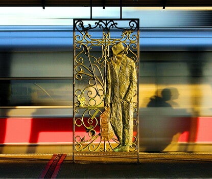 A train platform with, at center, a wrought-iron sculpture of a man wearing a suit and hat while holding a suitcase.