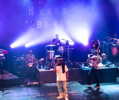 The Roots in performance on stage at the House of Blues — band members include (left to right) a saxophonist, trumpeter, keyboardist, guitarist, vocalist (Tariq "Black Thought" Trotter, wearing a white shirt, jeans, sunglasses and a dark hat while holding a microphone), drummer (Ahmir "Questlove" Thompson, behind the drum kit, wearing a black t-shirt), sousaphonist, and percussionist.