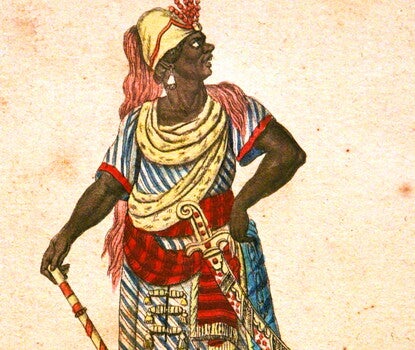 A Black man in a multicolored robe and cape, a gold hat with a red frill, and silver earrings, looking upward.