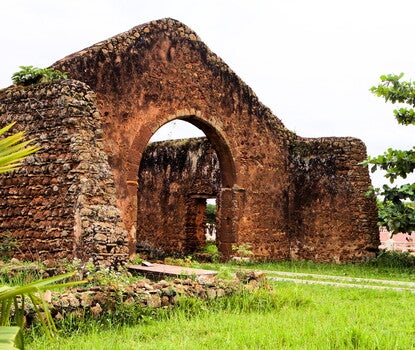 Ruins of a large brick cathedral (the roof no longer present), with a green tree at right.