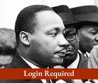 A black-and-white headshot of Martin Luther King Jr. preparing to speak into a bank of microphones as others look on. "Login Required" Message overlay.