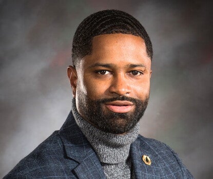 Marcus Nevius wearing a checked-stripe sport coat with a lapel pin over a gray turtleneck.
