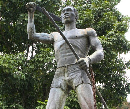 Metal of a shirtless man wearing shorts and holding a spear. His let wrist has a chain that has been broken.