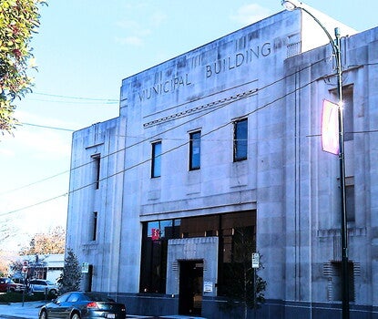 A large stone building with "MUNICIPAL BUILDING" carved above the front doors and flags of North Carolina, the United States, and Wilson on poles above the entrance. 
