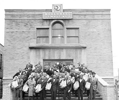 Black men in dark suits and ties (some neckties, some bowties) holding bundled stacks of newspapers on the steps of a brick building topped with a crescent and the words "Muhammad's Temple No. 2."
