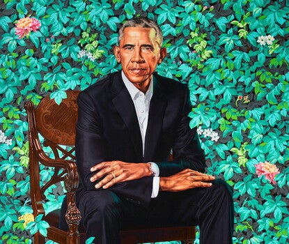 A portrait of Barack Obama sitting in a brown wooden chair wearing a black suit and white collared shirt. Surrounding President Obama are leaves and flowers of different varieties.