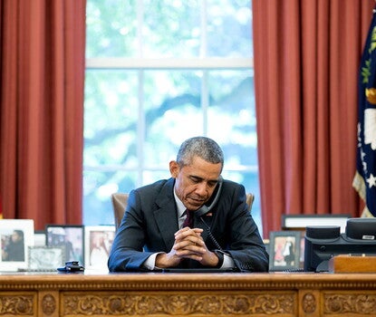 President Obama seated at his desk in the Oval Office, taking phone call. 