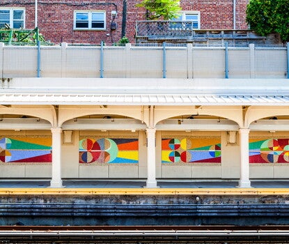 Four multicolored abstract mosaic panels on an outdoor subway platform.