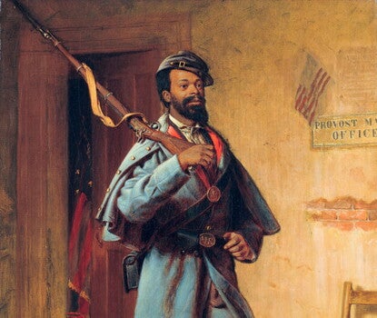 A Black soldier in a blue Union Army uniform (jacket, coat, pants, and hat), holding a rifle on his right shoulder with a slight smile on his face.