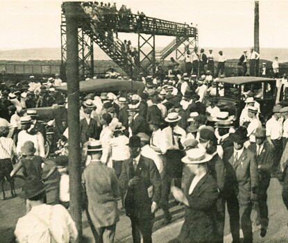 A black-and-white photograph of a large group of Black and White people congregating on a bridge, as cars attempt to pass.