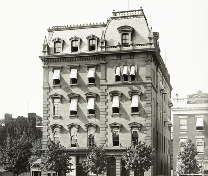 A black-and-white photograph of a five-story brick building with a mansard roof.