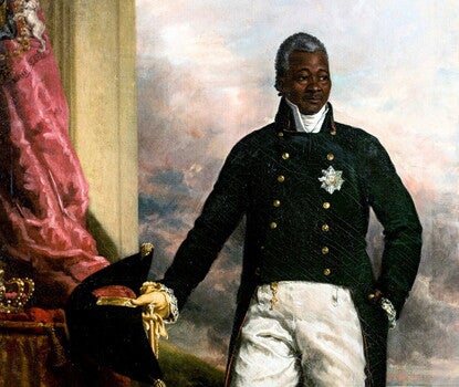 Henri Christophe, a Black man, in military uniform (blue double-breasted jacket with tails, white shirt, white pants, yellow boots), holding a sabre and dark hat in his right hand with his left in his jacket pocket. 