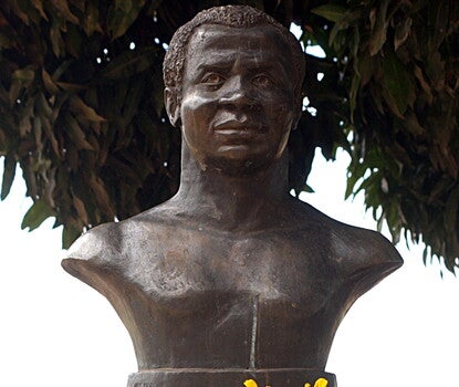 A metal bust of a man on a marble base, topped with two Black-eyed Susan flowers. The bust reads "Zumbi dos Palmares: O Líder Negro De Todas As Raças."