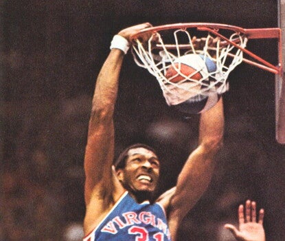 Roger Brown, a Black man wearing a blue basketball uniform, slam-dunking a red, white, and blue ABA basketball.