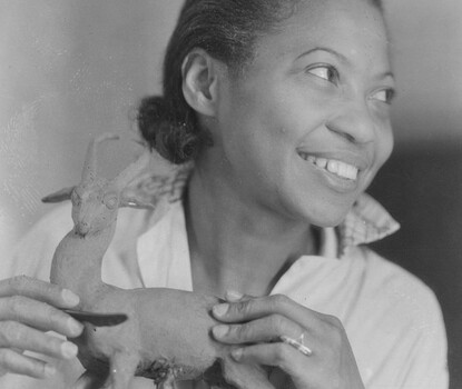 Augusta Savage, a Black woman, smiling and looking to her left as she holds a small sculpture of an antelope or similar creature in her hands.