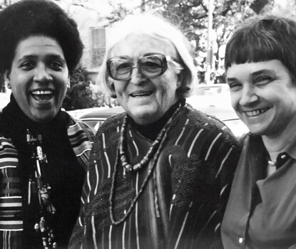 A black-and-white photograph of three women, Audre Lorde, a Black woman with an afro at left; Meridel Lesueur, a White woman with white hair and glasses in the center; and Adrienne Rich, a White woman with short black hair, at right.