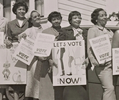A black-and-white photograph of several Black women in dresses holding signs in support of voter registration.