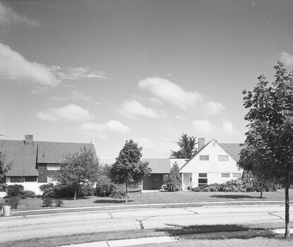 A black-and-white photograph of three suburban houses with a small tree in the foreground.