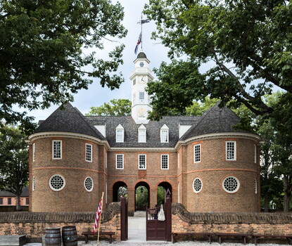 A brick building with two round sections on either side, connected via a colonnade topped by a white steeple and flagpole in front of a brick fence.